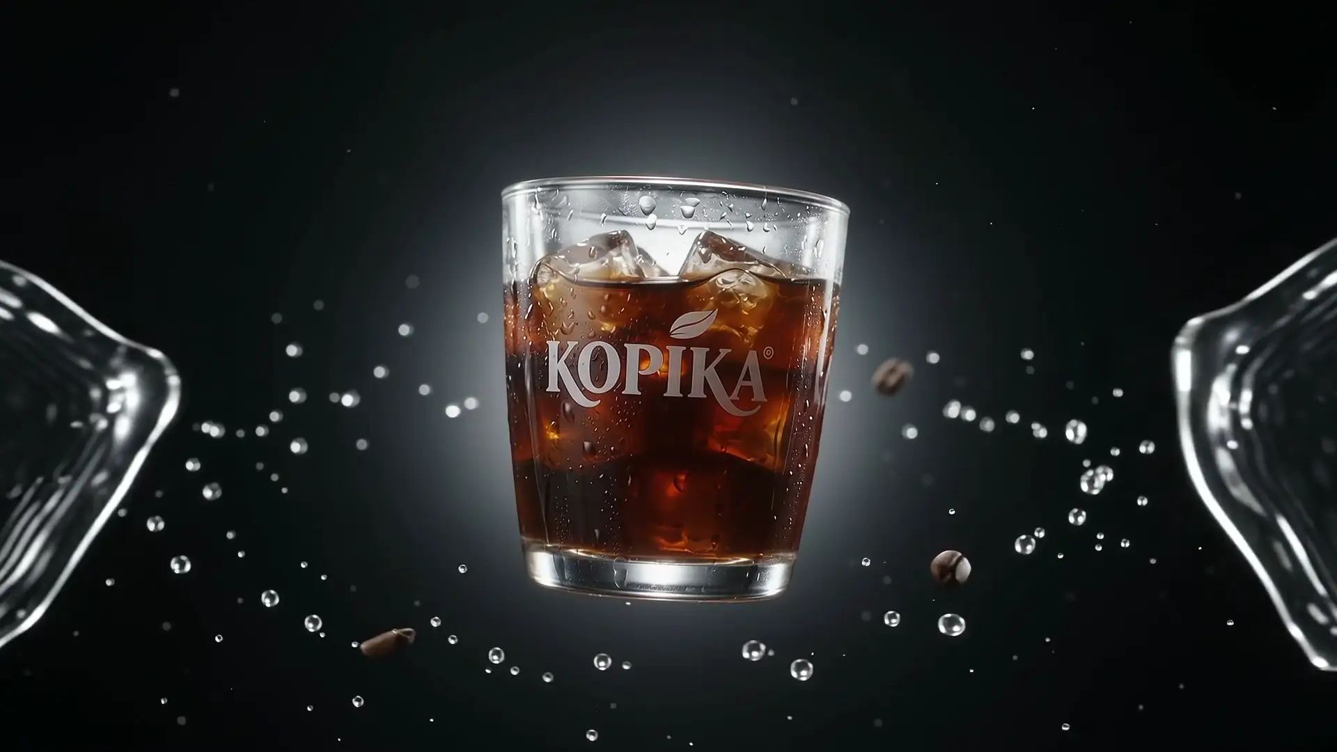 A glass of KOPIKA iced coffee hangs in the air on black. As you scroll, water and coffee beans splash around it.